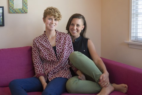 Caucasian lesbian couple smiling on sofa