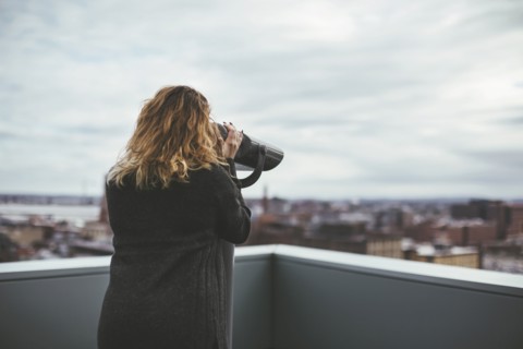 Caucasian woman on urban rooftop admiring cityscape with telescope