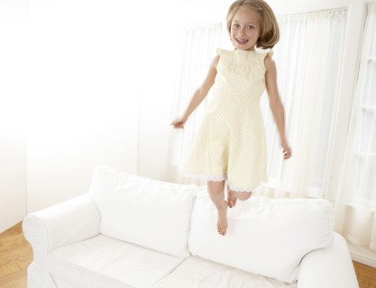 Caucasian girl jumping on sofa in living room
