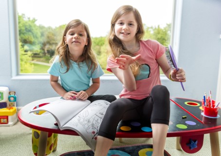 Caucasian sisters drawing at table in playroom