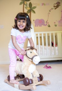 Girl riding rocking horse in nursery