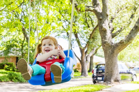 Caucasian girl playing on swing in front yard