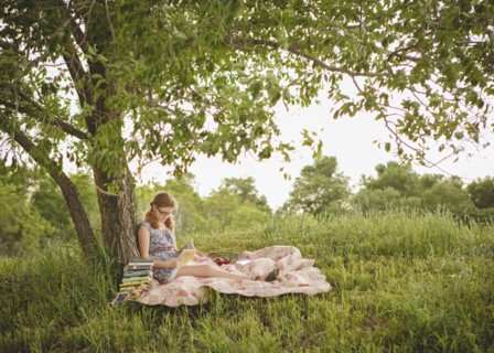Caucasian girl reading book under tree in field