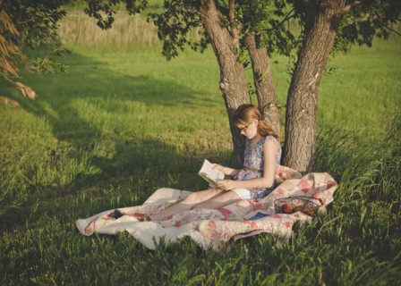 Caucasian girl reading book under tree in field