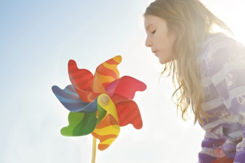 Caucasian girl playing with pinwheel under blue sky