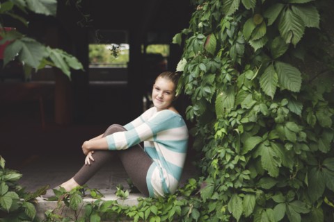 Caucasian teenage girl sitting at ivy wall