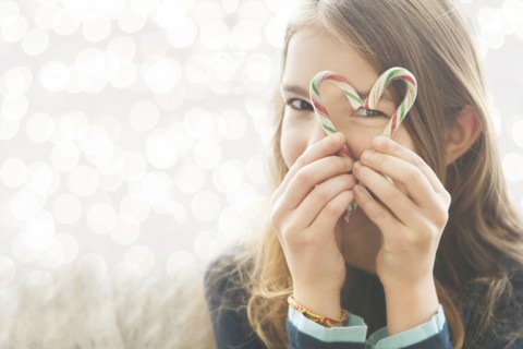 Caucasian girl looking through heart-shape with candy canes