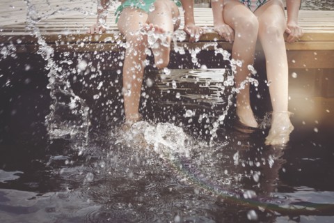 Caucasian girls splashing in lake from wooden dock