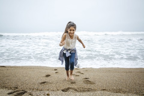 Hispanic girl walking barefoot on beach