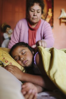 Hispanic grandmother tucking granddaughter into bed