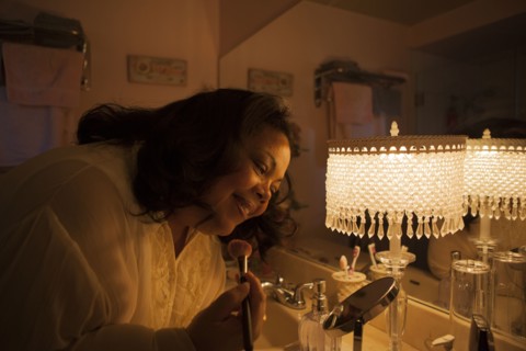 Woman applying makeup in bathroom mirror