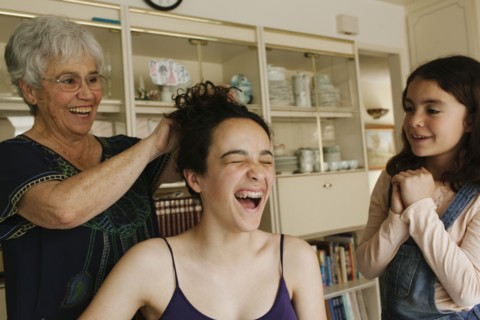 Grandmother styling hair of granddaughter in dining room