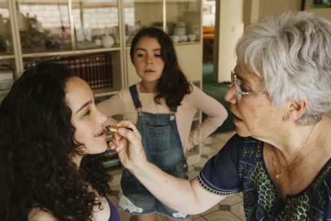 Grandmother applying lipstick to granddaughter in dining room
