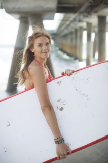 Woman carrying surfboard under boardwalk on beach