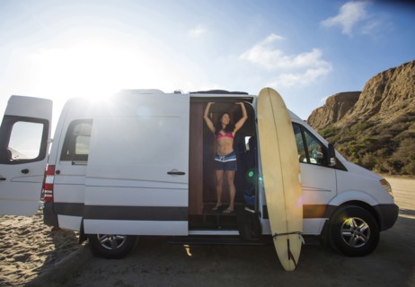 Hispanic surfer standing in van with surfboard