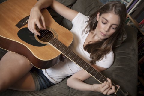 Caucasian woman playing guitar on sofa