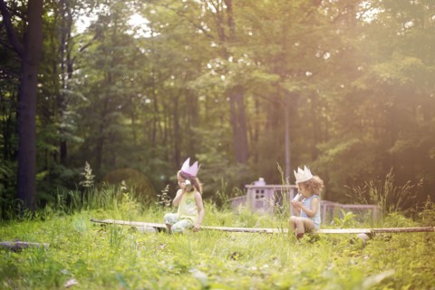 Girls playing telephone on wooden log in garden