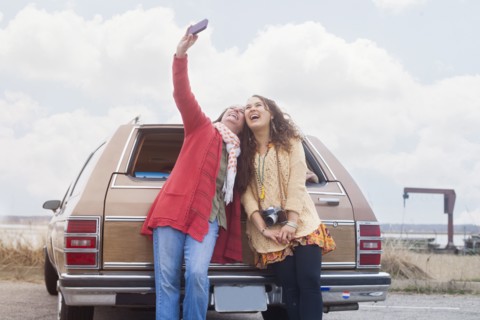 Caucasian mother and daughter taking selfie near car