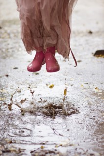 Caucasian girl in rain boots jumping in rain puddles