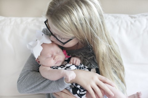 Caucasian girl kissing newborn sister on sofa