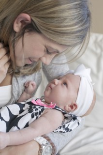 Caucasian mother kissing newborn daughter on sofa