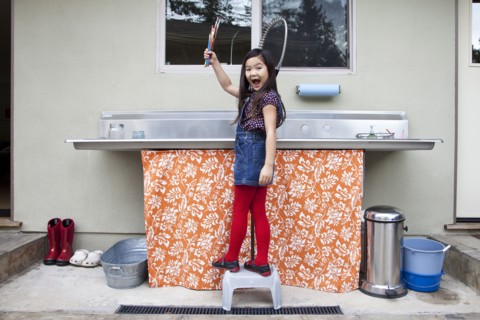 Mixed race girl showing clean paintbrushes at sink