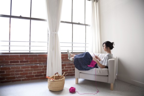 Taiwanese woman knitting in armchair near window