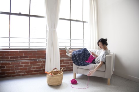 Taiwanese woman knitting in armchair near window