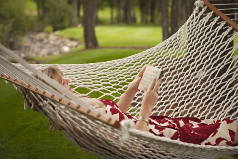 Woman reading book in backyard hammock