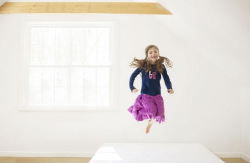 Caucasian girl jumping on bed