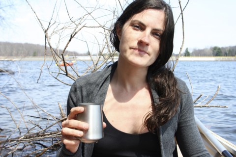 Woman drinking with metal cup in boat on lake