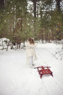 Caucasian girl pulling sled in snowy field