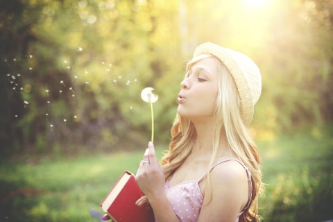 Woman blowing dandelion seeds in rural field