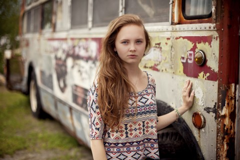 Caucasian teenage girl standing near dilapidated bus