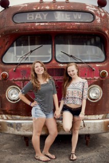 Smiling girls holding hands near dilapidated bus