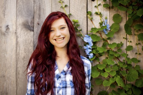 Woman smiling near wooden fence and ivy