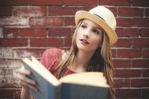 Girl reading book near brick wall
