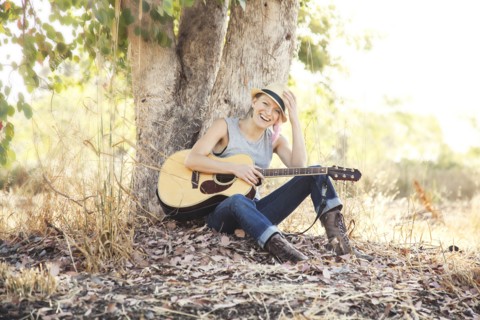 Caucasian musician holding guitar under tree