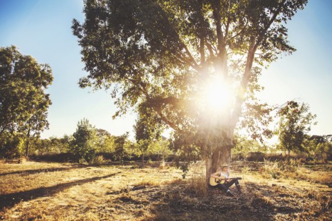 Caucasian musician playing guitar in rural field