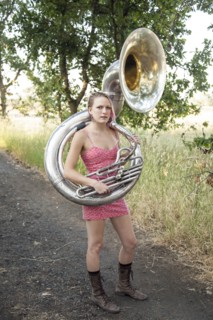 Caucasian musician carrying tuba on dirt path