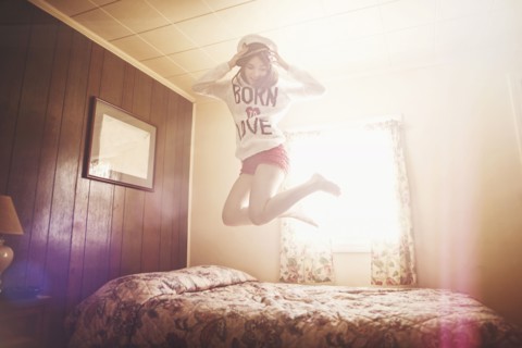 Caucasian girl in captain hat jumping on bed