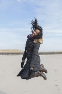 Woman in coat jumping for joy on beach