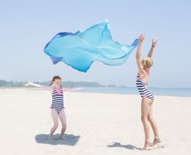 Caucasian girls playing with fabric on beach