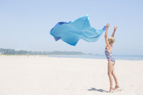 Caucasian girl playing with fabric on beach