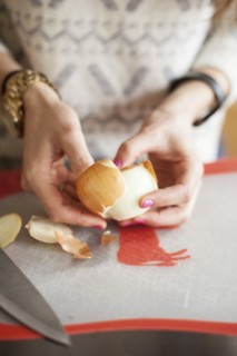 Close up of woman peeling onion on cutting board