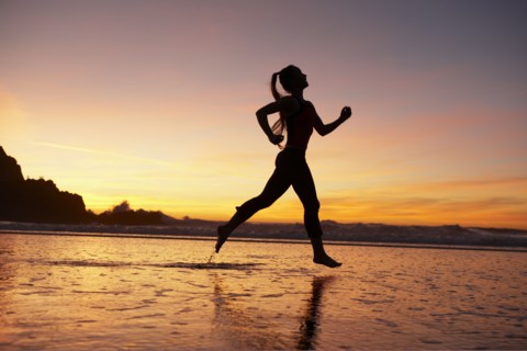 Silhouette of woman running on beach at sunset