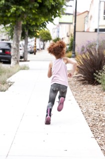 Rear view of girl running on city sidewalk