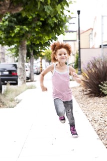 Smiling girl running on city sidewalk