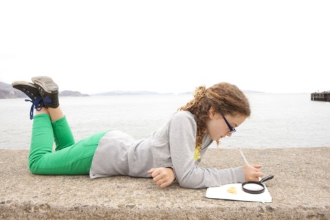 Caucasian girl doing homework on concrete wall over ocean