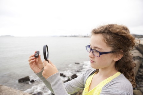Caucasian girl examining stone with magnifying glass